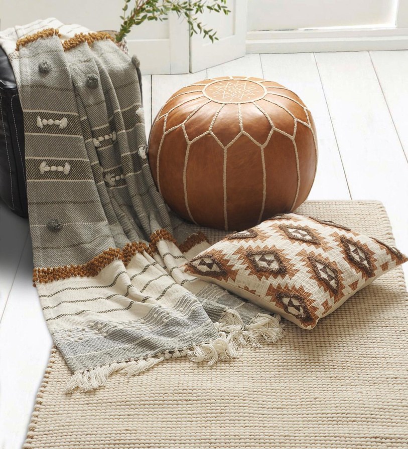 A home setting with a woven rug, patterned cushion and pouf